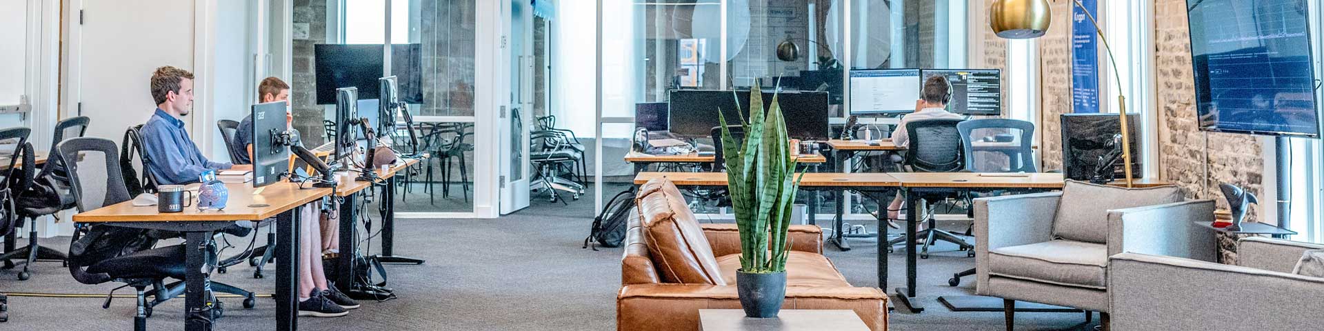 an open-concept moden office space with a lounge and empolyees sitting at their computer workstations