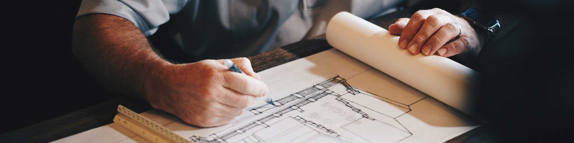 an architect is sketching a new designed on a roll of tracing paper held down at one end by a scale