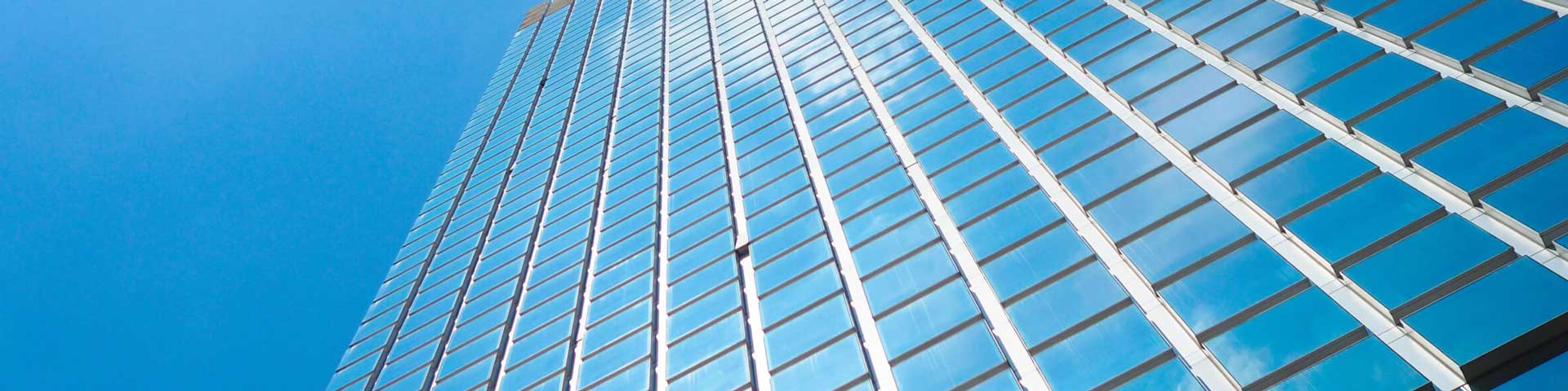 looking up at a glass clad skyscraper on a blue sky day with white clouds reflected in the glass.